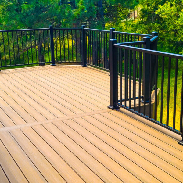Spacious wooden deck with black metal railings surrounded by greenery.